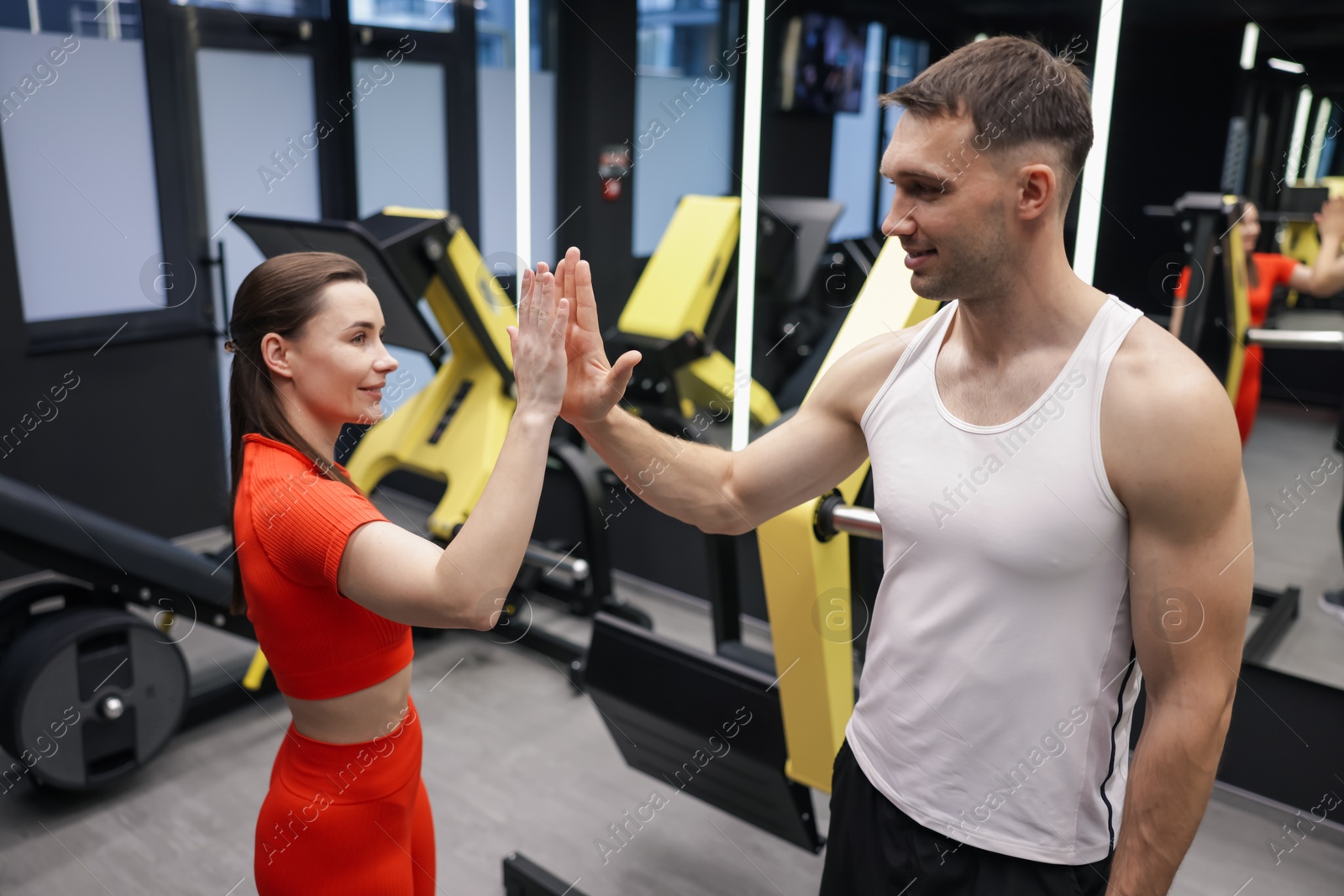 Young woman with professional personal trainer giving high five in gym Photo of Young woman with professional personal trainer giving high five in gym