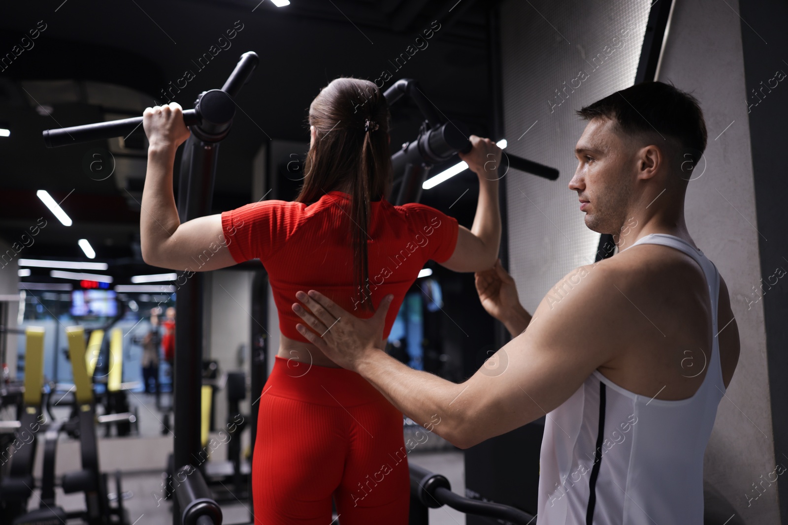 Young woman exercising with pull up machine with professional personal trainer in gym Photo of Young woman exercising with pull up machine with professional personal trainer in gym