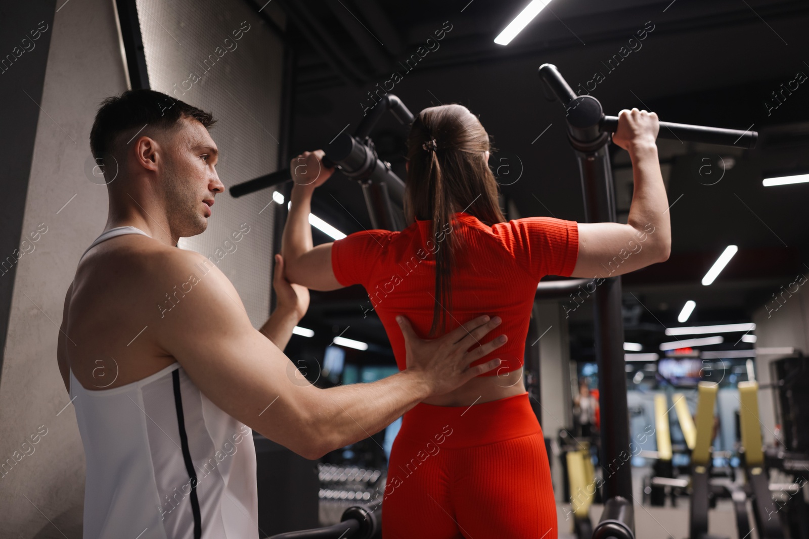 Young woman exercising with pull up machine with professional personal trainer in gym Photo of Young woman exercising with pull up machine with professional personal trainer in gym