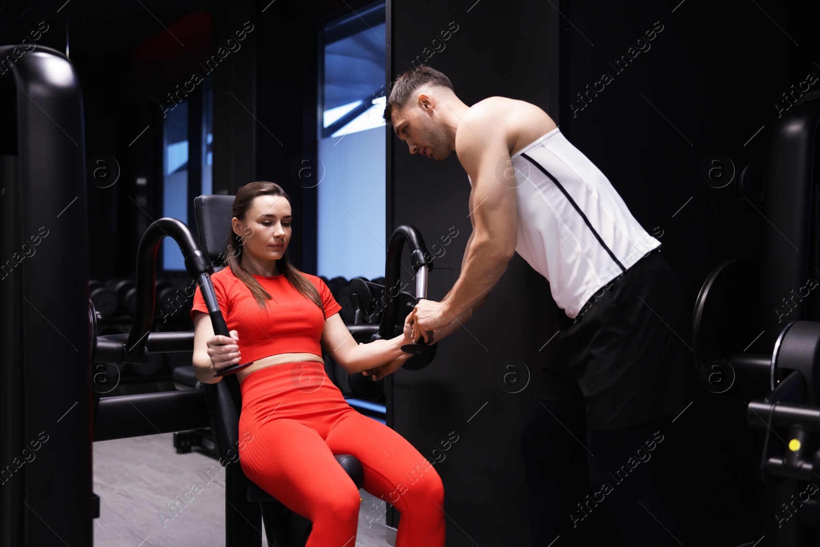 Photo of Young woman exercising with pull down machine professional personal trainer in gym