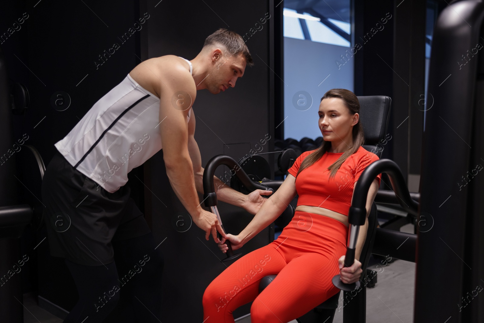 Photo of Young woman exercising with pull down machine professional personal trainer in gym