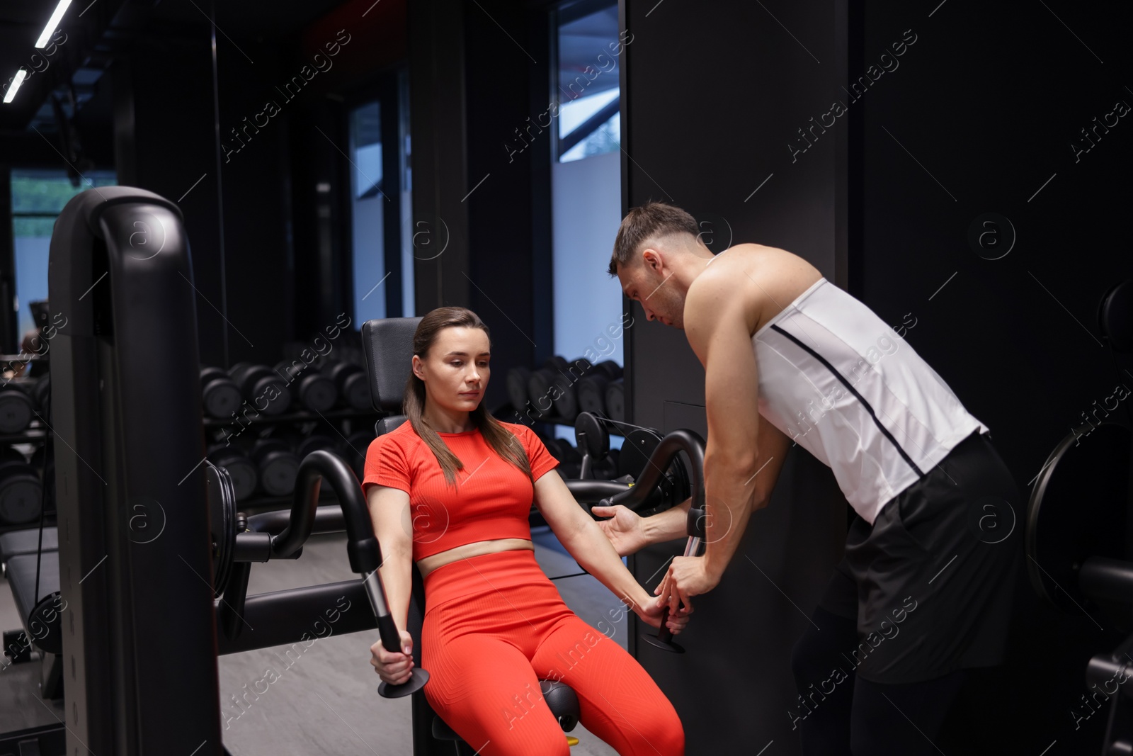 Photo of Young woman exercising with pull down machine professional personal trainer in gym