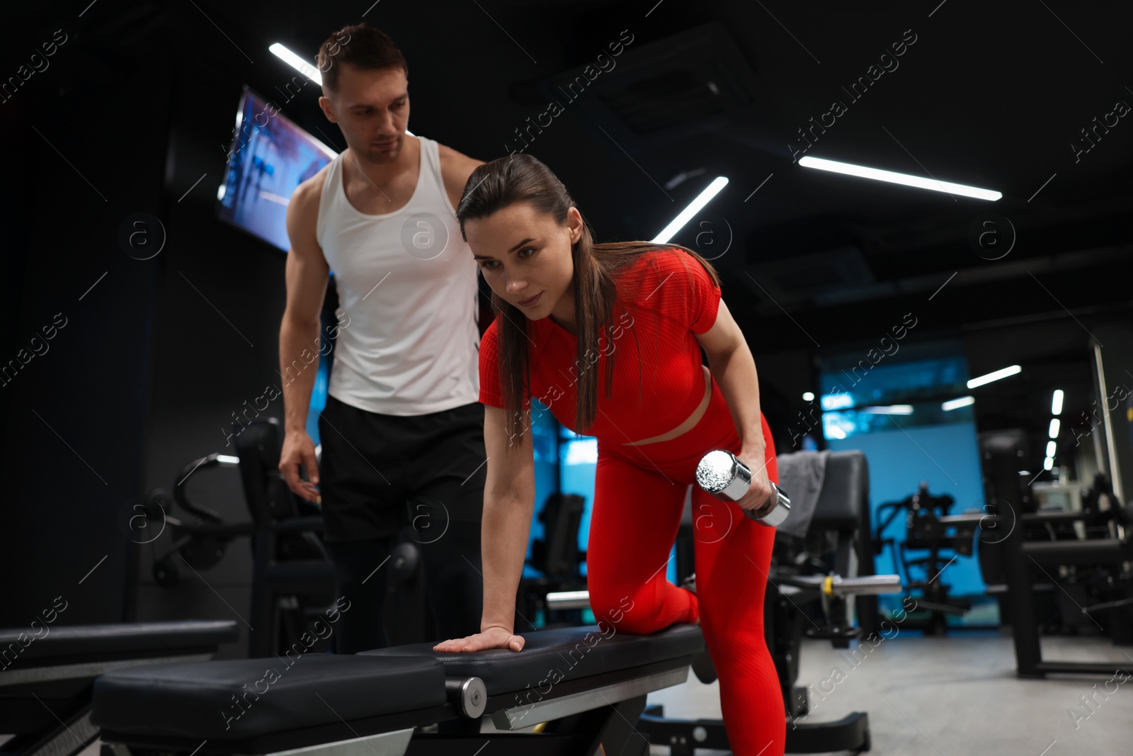 Photo of Young woman exercising with dumbbells with professional personal trainer in gym