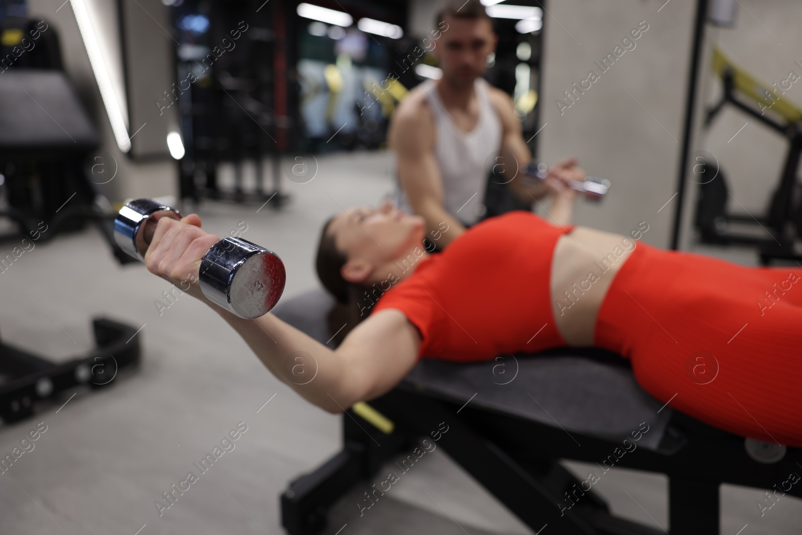 Photo of Young woman exercising with dumbbells with professional personal trainer in gym, selective focus