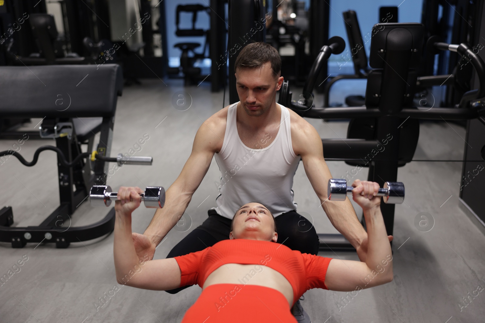 Photo of Young woman exercising with dumbbells with professional personal trainer in gym