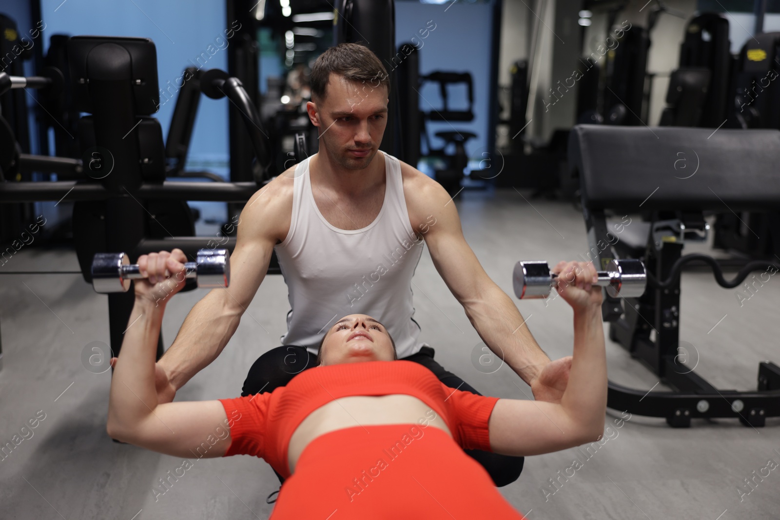 Photo of Young woman exercising with dumbbells with professional personal trainer in gym