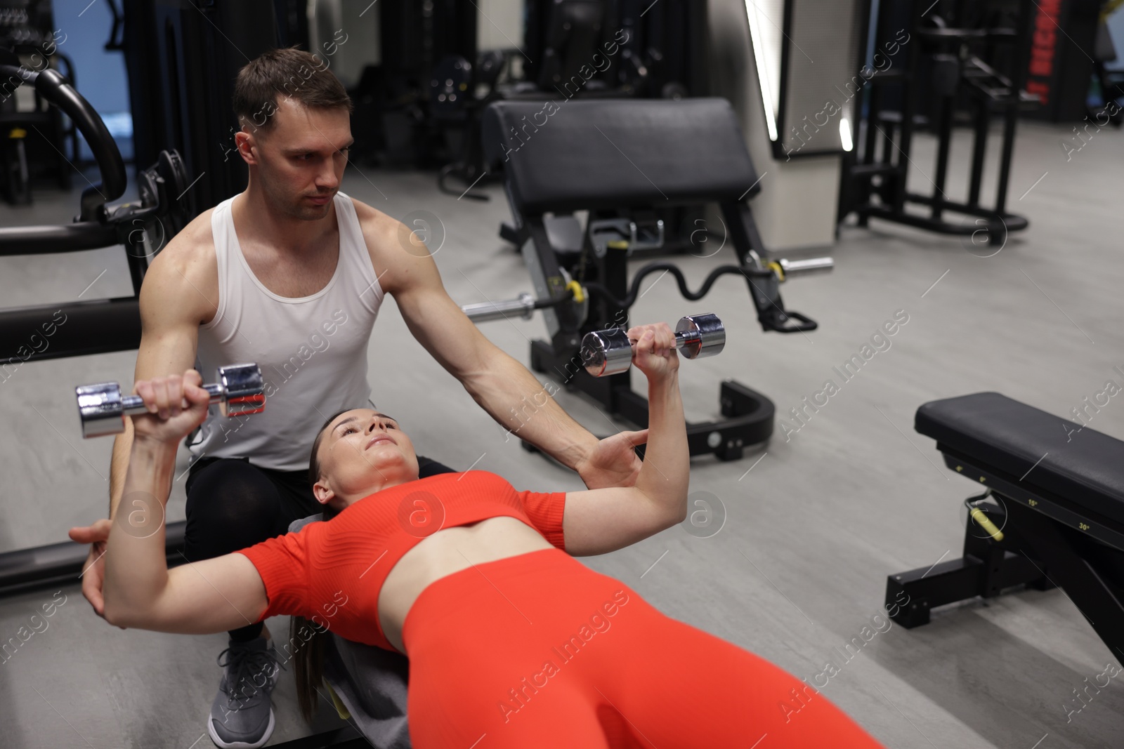 Young woman exercising with dumbbells with professional personal trainer in gym Photo of Young woman exercising with dumbbells with professional personal trainer in gym