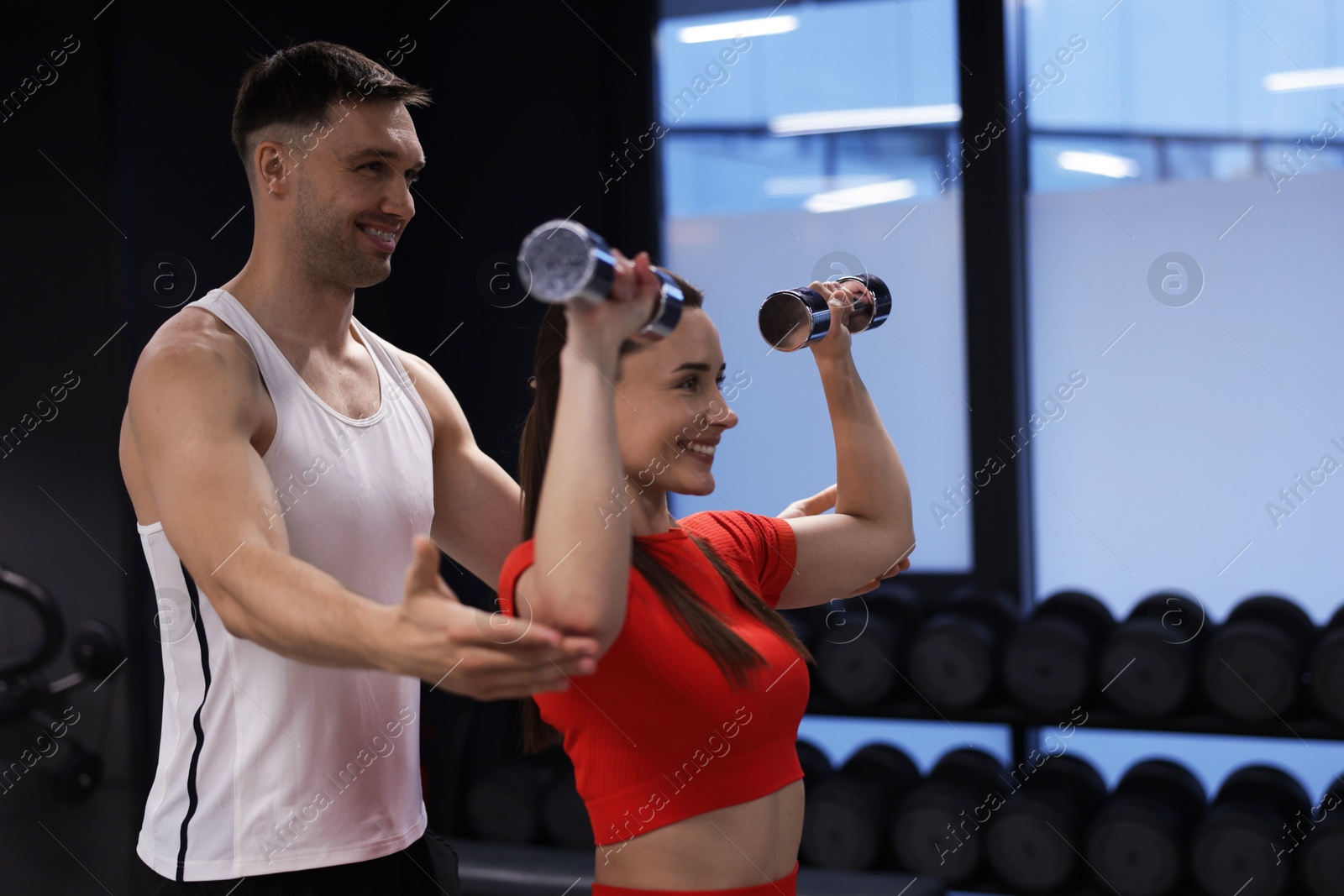 Young woman exercising with dumbbells with professional personal trainer in gym, space for text Photo of Young woman exercising with dumbbells with professional personal trainer in gym, space for text