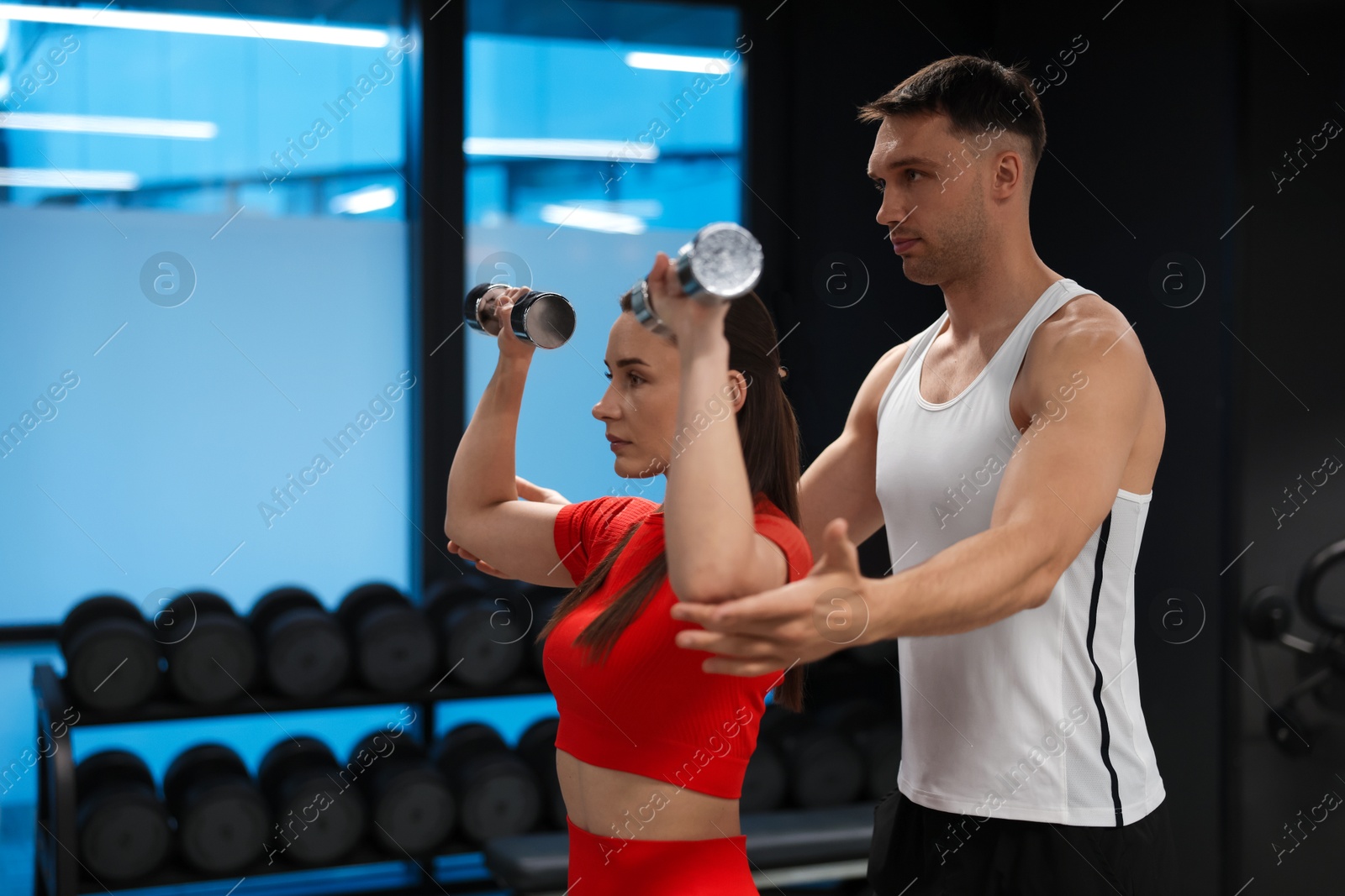 Young woman exercising with dumbbells with professional personal trainer in gym, space for text Photo of Young woman exercising with dumbbells with professional personal trainer in gym, space for text