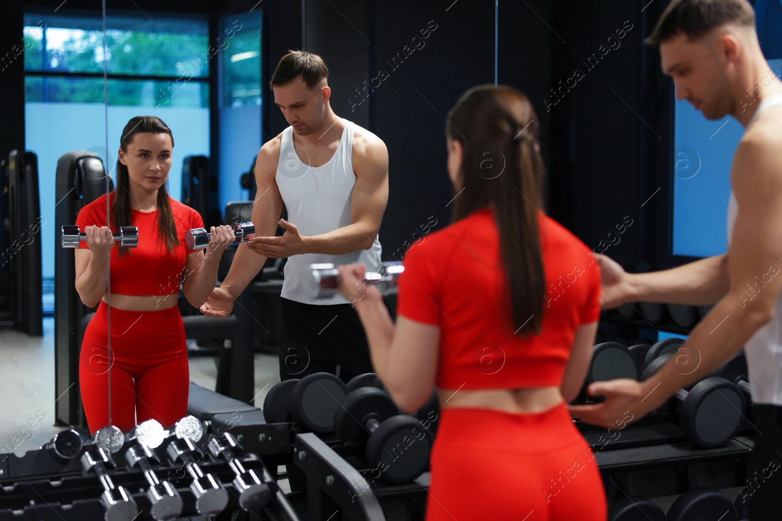 Young woman exercising with dumbbells with professional personal trainer in gym Photo of Young woman exercising with dumbbells with professional personal trainer in gym