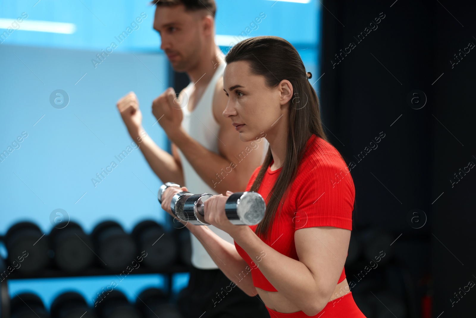 Young woman exercising with dumbbells with professional personal trainer in gym, selective focus Photo of Young woman exercising with dumbbells with professional personal trainer in gym, selective focus