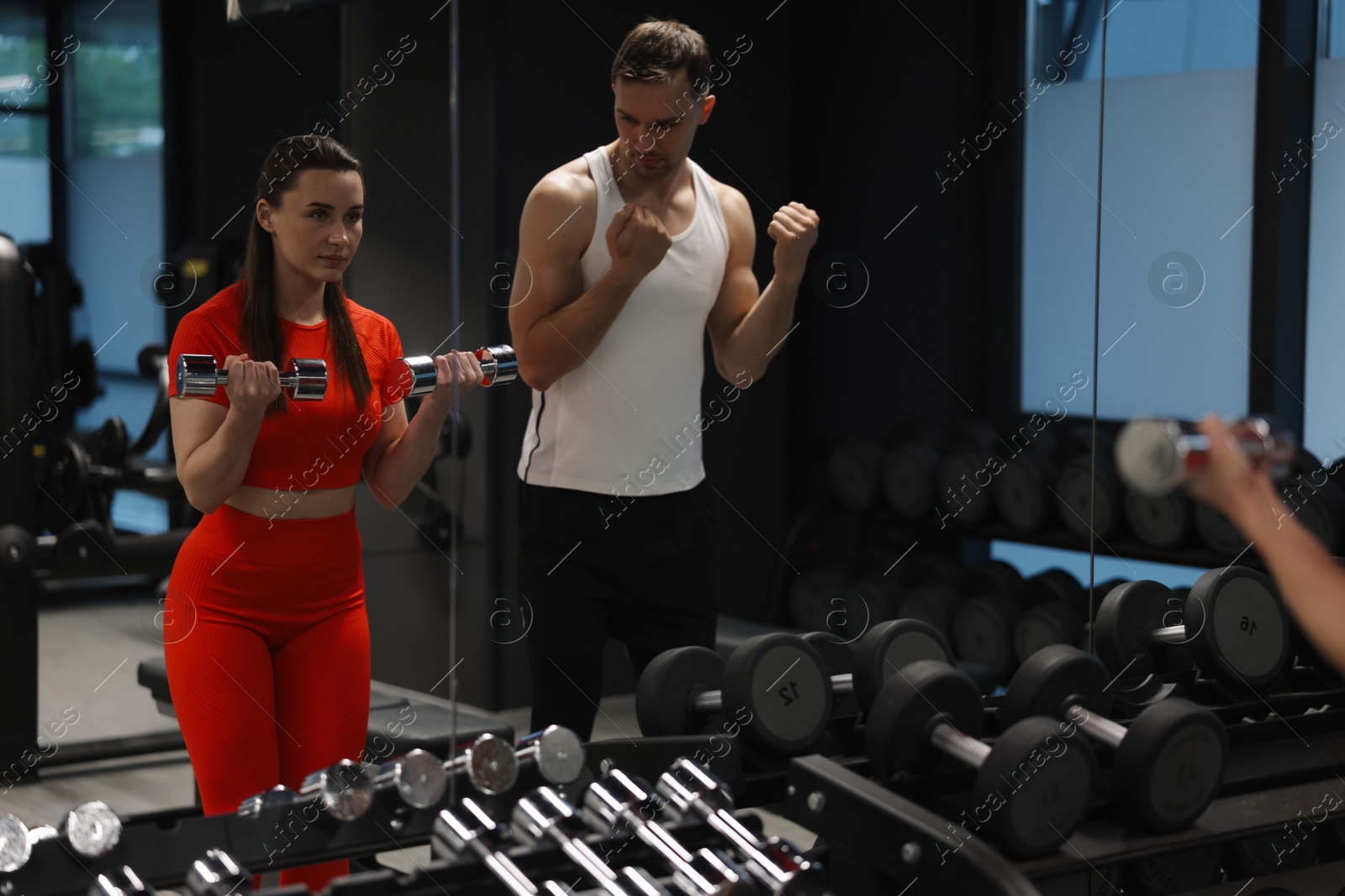 Young woman exercising with dumbbells with professional personal trainer in gym Photo of Young woman exercising with dumbbells with professional personal trainer in gym