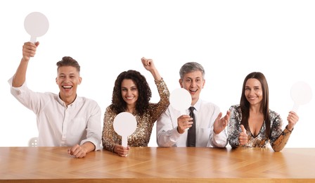 Photo of Panel of happy judges with blank score signs at table on white background