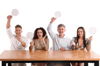 Photo of Panel of happy judges with blank score signs at table on white background