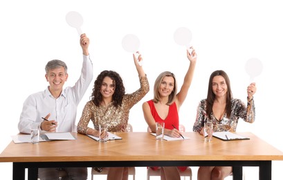 Photo of Panel of happy judges with blank score signs at table on white background