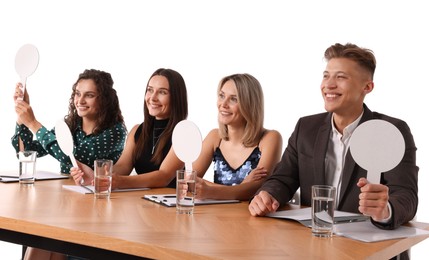 Photo of Panel of happy judges with blank score signs at table on white background