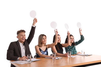 Photo of Panel of happy judges with blank score signs at table on white background