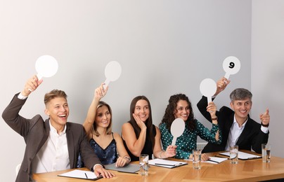 Photo of Panel of happy judges voting with score signs at table near grey wall