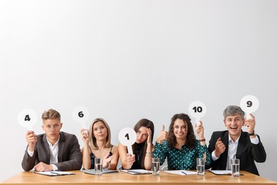 Photo of Panel of judges voting with score signs at table against light grey background