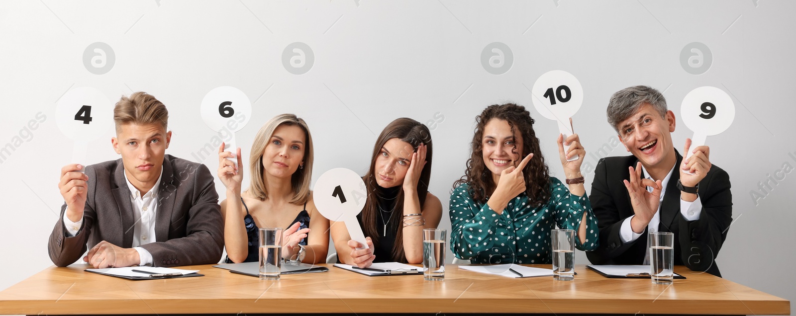 Panel of emotional judges voting with score signs at table against light grey background Photo of Panel of emotional judges voting with score signs at table against light grey background