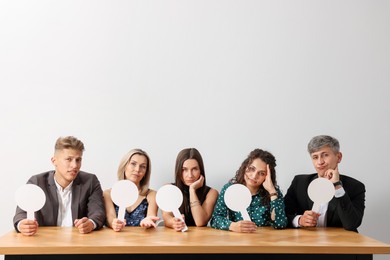 Photo of Panel of judges voting with score signs at table against light grey background