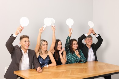 Photo of Panel of happy judges voting with blank score signs at table near grey wall