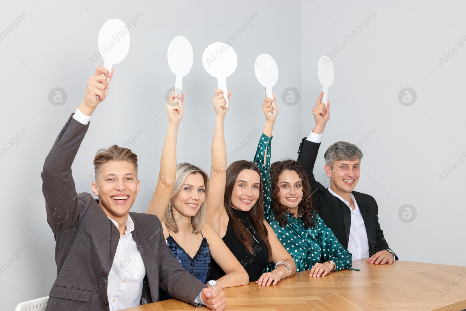Panel of happy judges voting with blank score signs at table near grey wall Photo of Panel of happy judges voting with blank score signs at table near grey wall