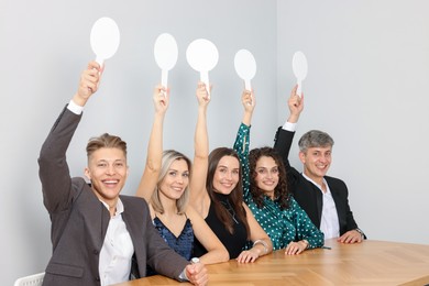 Photo of Panel of happy judges voting with blank score signs at table near grey wall