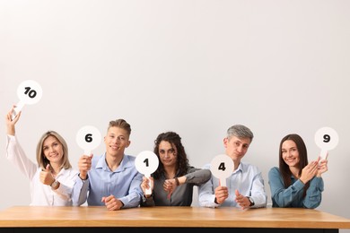 Photo of Panel of emotional judges voting with blank score signs at table against light grey background