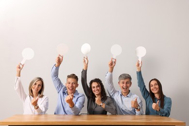 Photo of Panel of emotional judges voting with blank score signs at table against light grey background