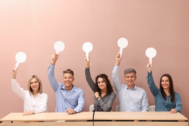 Photo of Panel of happy judges voting with blank score signs at tables against beige background