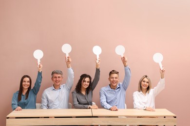 Photo of Panel of happy judges voting with blank score signs at tables against beige background