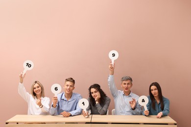 Photo of Panel of emotional judges voting with score signs at tables against beige background
