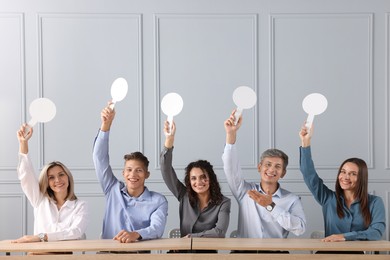 Photo of Panel of happy judges voting with blank score signs at tables near grey wall