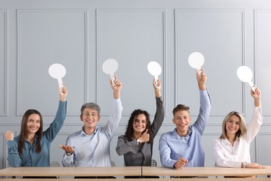 Photo of Panel of happy judges voting with blank score signs at tables near grey wall