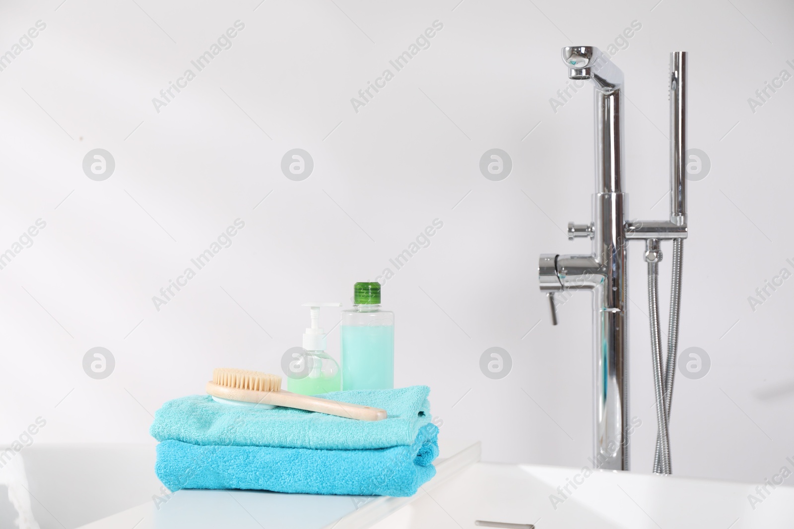 Photo of White board with soft towels, brush and cosmetic products on tub indoors