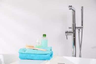 Photo of White board with soft towels, brush and cosmetic products on tub indoors