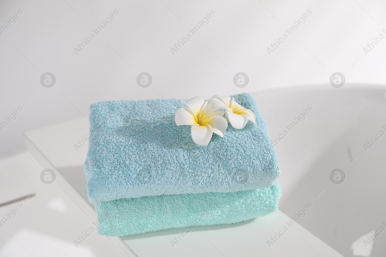 White board with soft towels and plumeria flowers on tub indoors Photo of White board with soft towels and plumeria flowers on tub indoors