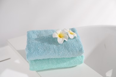 Photo of White board with soft towels and plumeria flowers on tub indoors