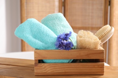 Photo of Soft towels, brush, loofah and flowers on wooden board indoors, closeup