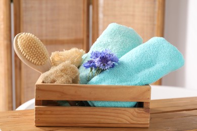 Photo of Soft towels, brush, loofah and flowers on wooden board indoors, closeup