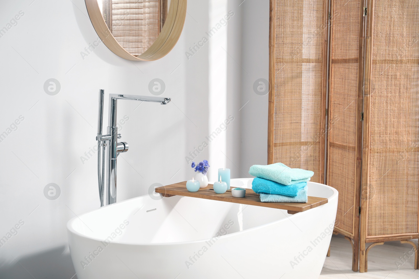 Wooden board with soft towels, sea salt, flowers and burning candles on tub in bathroom Photo of Wooden board with soft towels, sea salt, flowers and burning candles on tub in bathroom