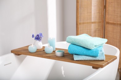 Photo of Wooden board with soft towels, sea salt, flowers and candles on tub in bathroom