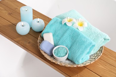 Photo of Wooden board with soft towels, sea salt, soap, plumeria flowers and candles on tub, above view
