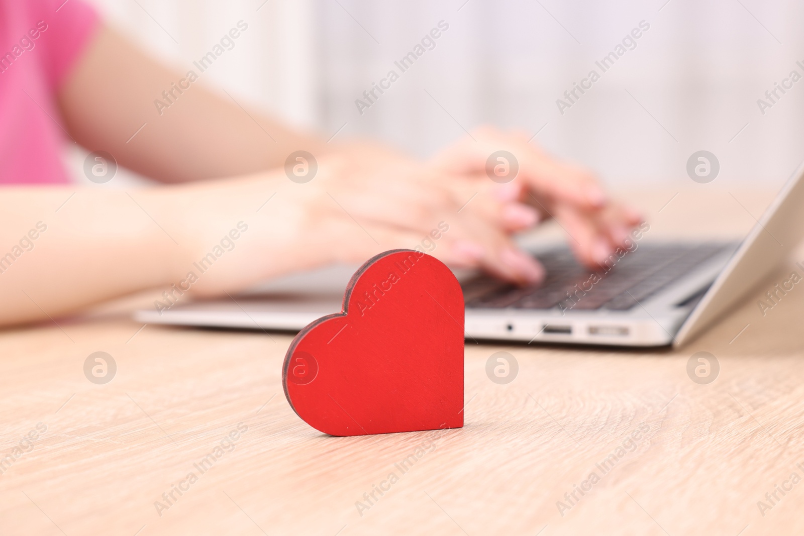 Online dating site. Woman using laptop at table indoors, focus on decorative heart Photo of Online dating site. Woman using laptop at table indoors, focus on decorative heart
