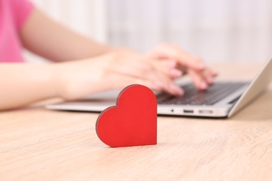 Photo of Online dating site. Woman using laptop at table indoors, focus on decorative heart