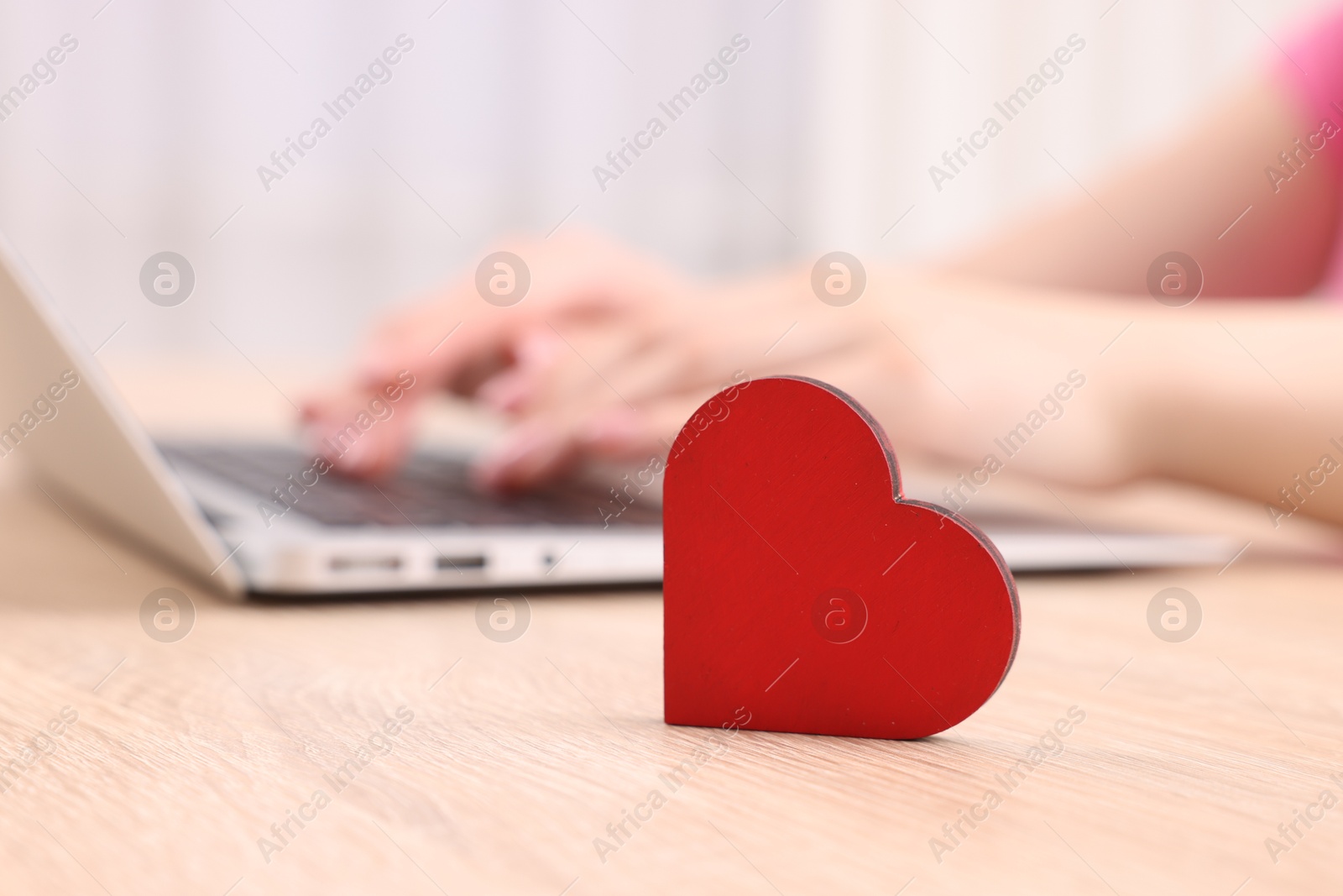 Online dating site. Woman using laptop at table indoors, focus on decorative heart Photo of Online dating site. Woman using laptop at table indoors, focus on decorative heart