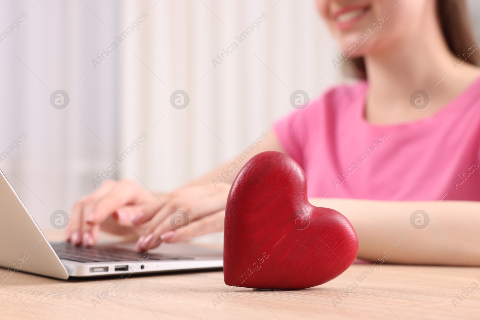 Online dating site. Woman using laptop at table indoors, focus on decorative heart Photo of Online dating site. Woman using laptop at table indoors, focus on decorative heart