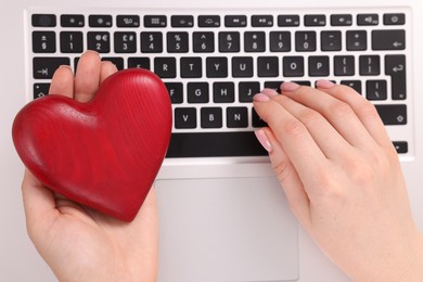 Photo of Online dating site. Woman with decorative heart using laptop, top view