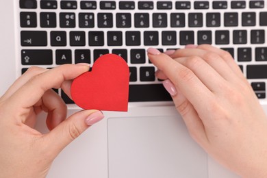 Photo of Online dating site. Woman with decorative heart using laptop, top view